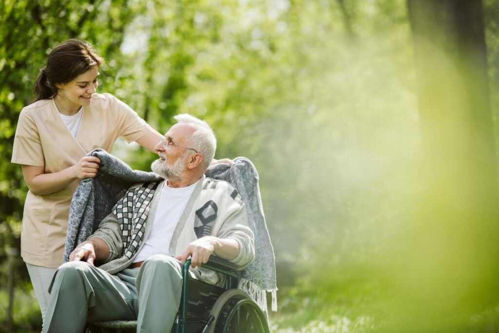 Caregiver helping an elderly man in a wheelchair stay comfortable outdoors, highlighting personalized senior care and mobility support based on individual needs.
