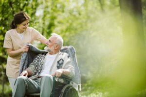 Caregiver helping an elderly man in a wheelchair stay comfortable outdoors, highlighting personalized senior care and mobility support based on individual needs.