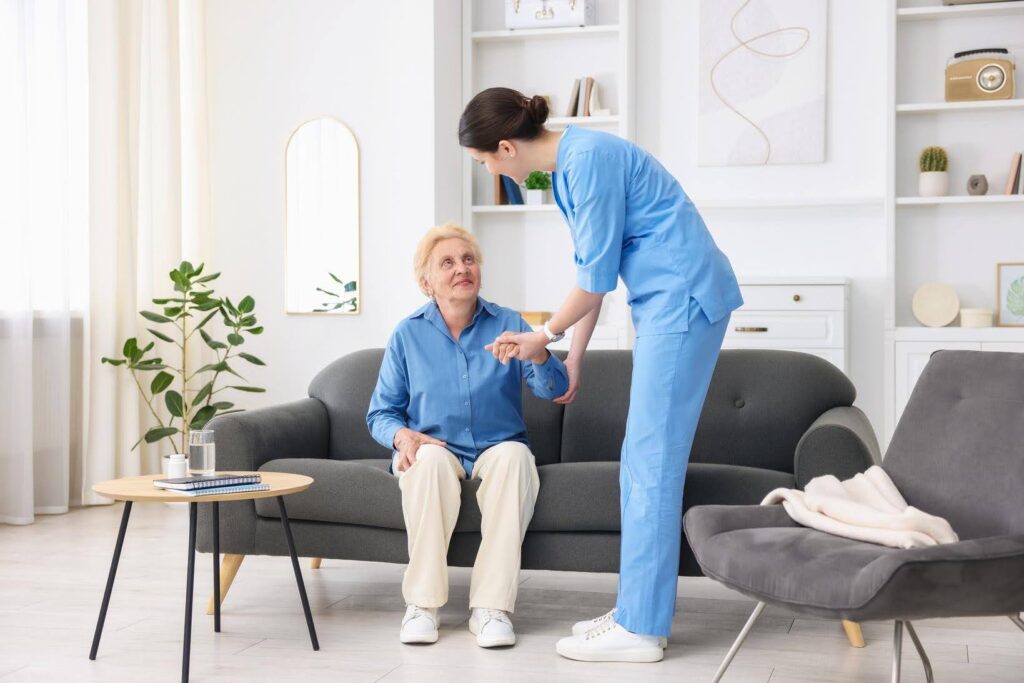 Caregiver assisting an elderly woman from a sofa, highlighting how personalized home care schedules support an aging parent's daily needs and independence.